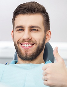 Man giving a thumbs up in the dental chair after tooth replacement with dental implants