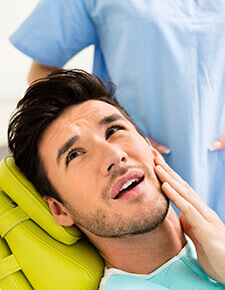 Young man in dental chair holding cheek before T M J therapy