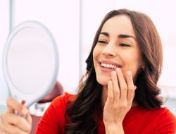 Woman in white tanktop brushing teeth at bathroom mirror