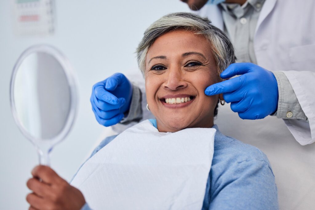 Patient smiling while holding small mirror with dentist